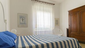 Ein Schlafzimmer mit einem Bett, einem Sessel, einem Holzschrank und zwei gerahmten Bildern an der Wand.