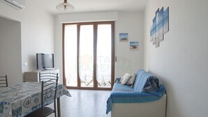Una habitación pequeña y luminosa con una mesa de comedor, un sofá y una televisión.