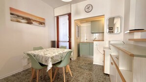 Une pièce comprenant une table à manger, des chaises, un coin cuisine et une horloge au mur.