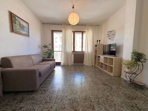 Un soggiorno con un divano, una TV su un mobile in legno, una lampada a sospensione e un quadro appeso al muro.