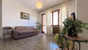 Un salon avec un canapé, une table sur laquelle est posée une plante, un radiateur et une fenêtre avec des rideaux.