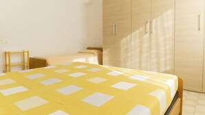 A bedroom with a bed, a wooden wardrobe, and a small table. - Alba apartment in Follonica (Follonica)