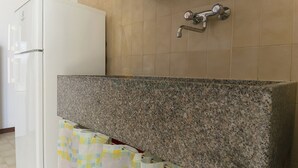Cuina amb taulell de granat, nevera blanca i aixeta fixada a la paret.