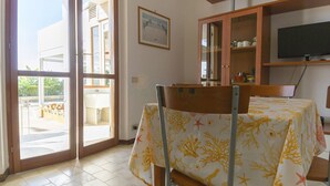 Una habitació amb una taula de dinar coberta amb un mantell, una cadira, un armari amb portes de vidre i un televisor penjat a la paret.