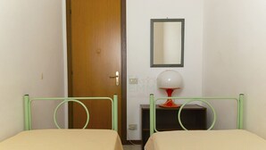 Una habitació amb dos llits, una porta de fusta, un mirall i una taula amb una làmpada.