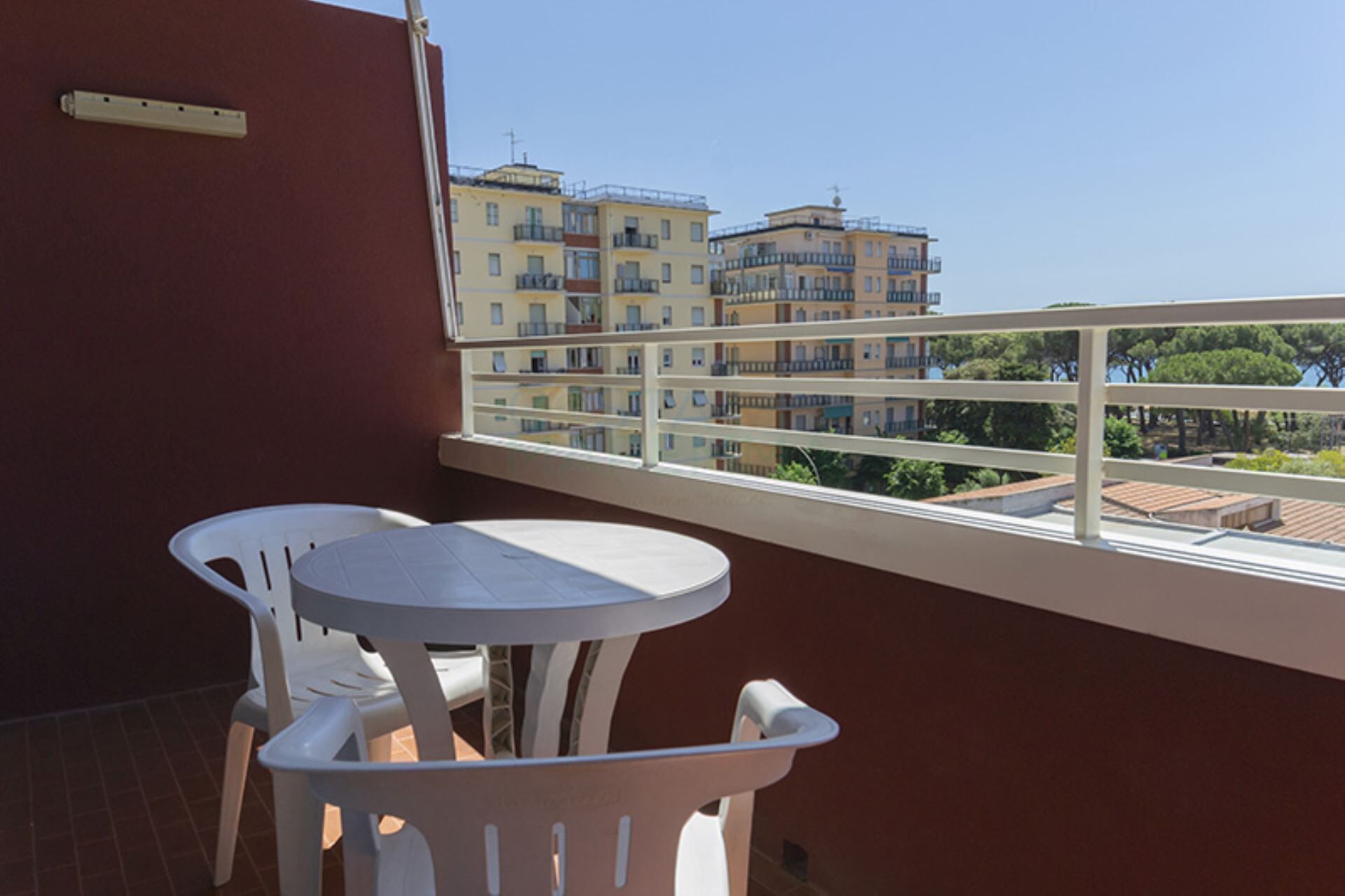 Un balcon avec une table et des chaises blanches, une vue sur des immeubles à plusieurs étages et une balustrade.