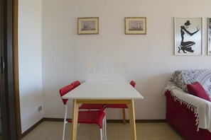 Una habitación con una mesa blanca y sillas rojas, un sofá rojo, y dos cuadros en la pared.