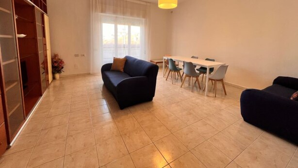 A living room with a sofa, a dining table with chairs, a hanging light fixture, and a window with curtains. - Fiume apartment in Follonica (Follonica)