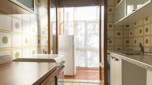 A kitchen with a refrigerator, a sink, and a window with a view of trees. - Pini apartment in Follonica (Follonica)