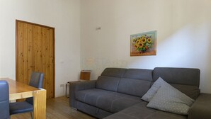 Ett vardagsrum med en trädörr, en grå soffa, ett litet bord och en målning av solrosor.