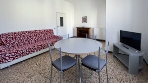 A modern living room with a round table, four chairs, a red patterned sofa, a television, and a fireplace. - Papavero apartment in Follonica (Follonica)