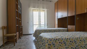 A bedroom with two beds, a chair, a wardrobe, and a window with curtains. - Salvia apartment in Follonica (Follonica)