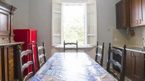 Ein Esszimmer mit einem für vier Personen gedeckten Tisch, Holzstühlen, einem roten Kühlschrank und einem Fenster mit geöffneten Läden.