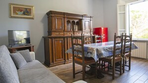 Ein Wohnzimmer mit grauem Sofa, einem Holzespeisetisch mit Stühlen, einem roten Kühlschrank und einem Fernseher auf einem Schrank.