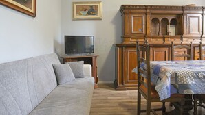 Ein Wohnzimmer mit Sofa, Fernseher auf einem Schrank, Esstisch mit Stühlen und einem Holzschrank.