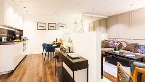 A modern kitchen with white cabinets, a dining area with a black table, and a living room with a sofa and coffee table. - LE MAY AP4338 By Riviera Holiday Homes (Villefranche-sur-Mer)