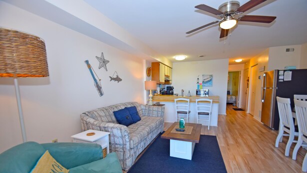 A living room with a sofa, a coffee table, and a ceiling fan. There is a kitchen area in the background. - Raffles 206-Bayside 127th St, Free WiFi, Pool, W/D, AC (Ocean City)