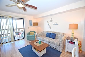 A living room with a ceiling fan, a sofa, a coffee table, a lamp, and a small cabinet. - Raffles 206-Bayside 127th St, Free WiFi, Pool, W/D, AC (Ocean City)