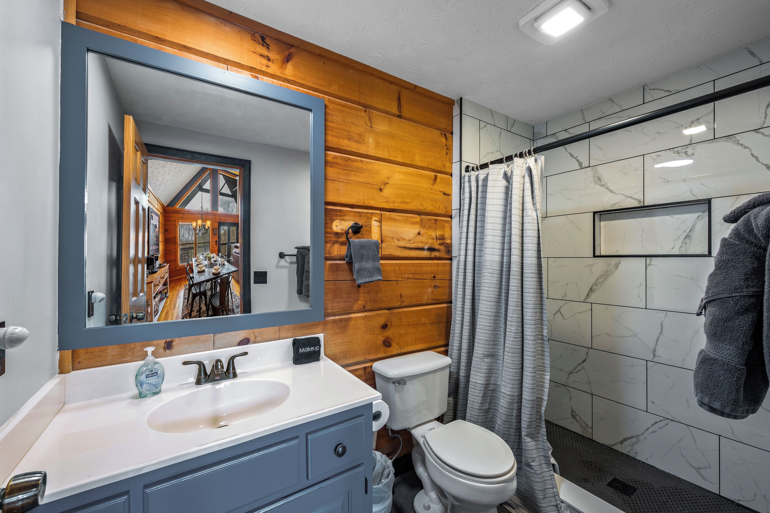 Un baño con pared de madera, un espejo grande, un lavabo, un inodoro y una ducha.