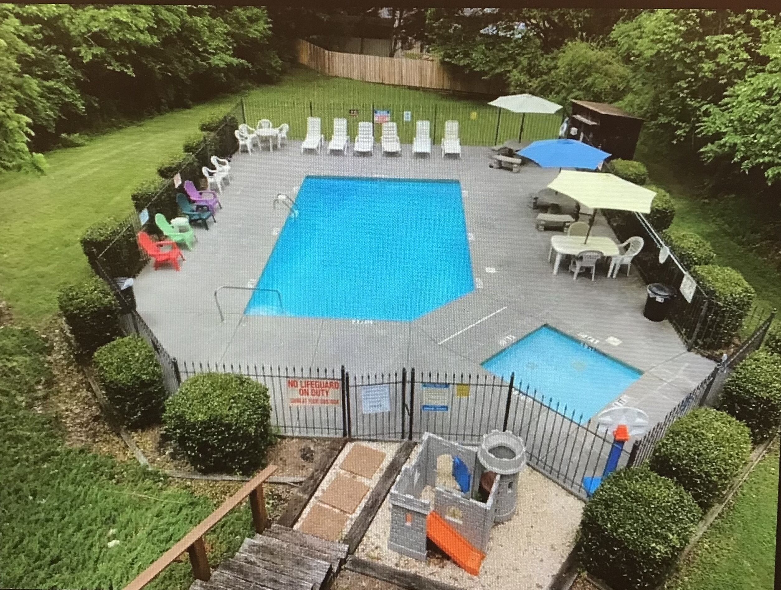 Una piscina rectangular con un borde pavimentado, sillones de descanso y una estación de salvavidas.