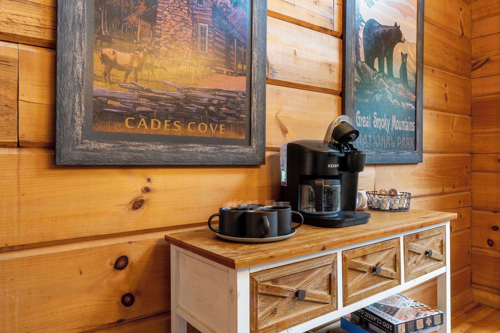 Een houten blokhut van binnen, met een koffiehoek, fotolijstjes met natuurfoto's en een boek op het onderste plankje.