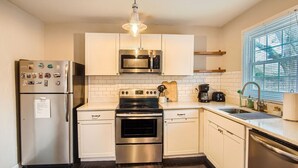 A modern kitchen with stainless steel appliances, white cabinetry, and a window with blinds. - 1429 Lanvale · Quaint Boho Retreat Near Downtown - Pet Friendly (Atlanta)