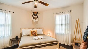A bedroom with a bed, a ceiling fan, a bedside table with a lamp, and a wooden ladder. - 1429 Lanvale · Quaint Boho Retreat Near Downtown - Pet Friendly (Atlanta)