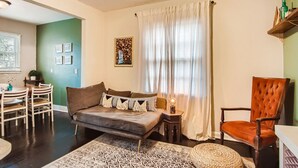 A living room with a sofa, a chair, a dining table, and a rug. - 1429 Lanvale · Quaint Boho Retreat Near Downtown - Pet Friendly (Atlanta)