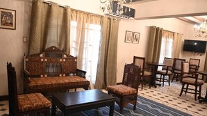 Una sala de estar tradicional con un sofá estampado, un reposapiés a juego y una mesa de centro. Hay un televisor montado en la pared y un candelabro.