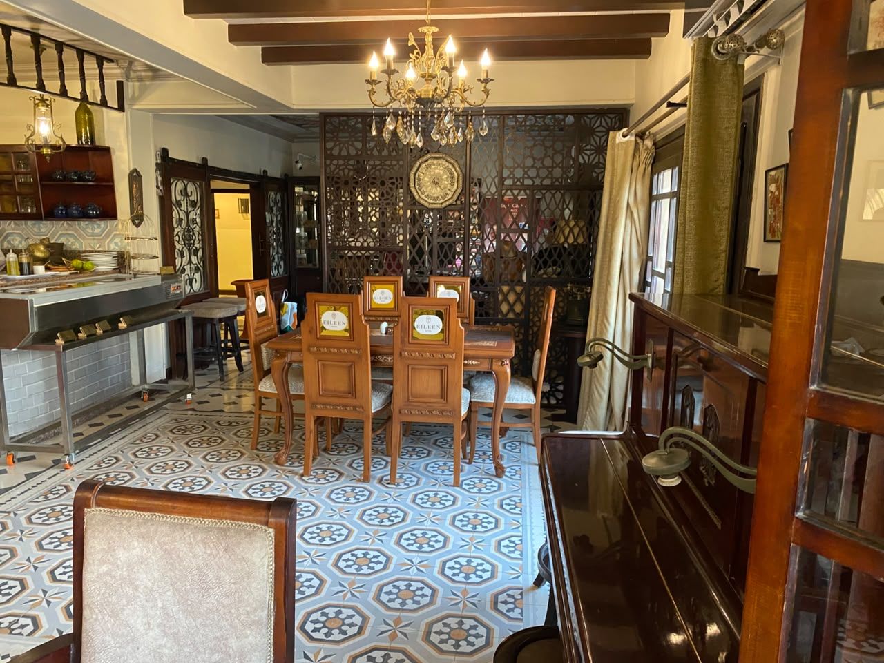 A dining area with a patterned floor, wooden chairs, a chandelier, and a bar area with shelves.