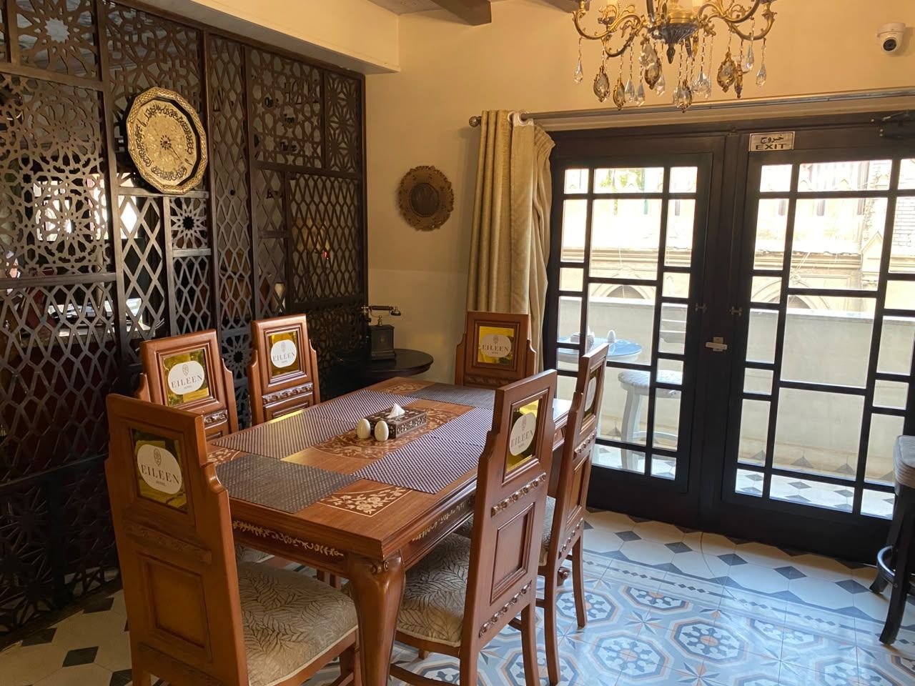 A dining area with a wooden table and chairs, a chandelier, and a view through a glass door.