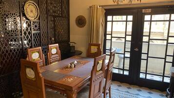 A dining area with a wooden table and chairs, a chandelier, and a view through a glass door.