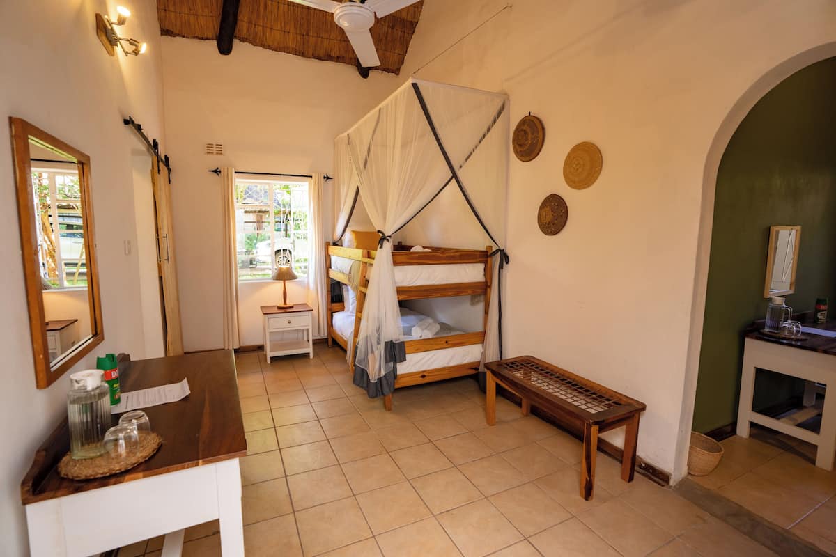 A room with a wooden bunk bed, a small table with a basket, a mirror, and a ceiling fan.