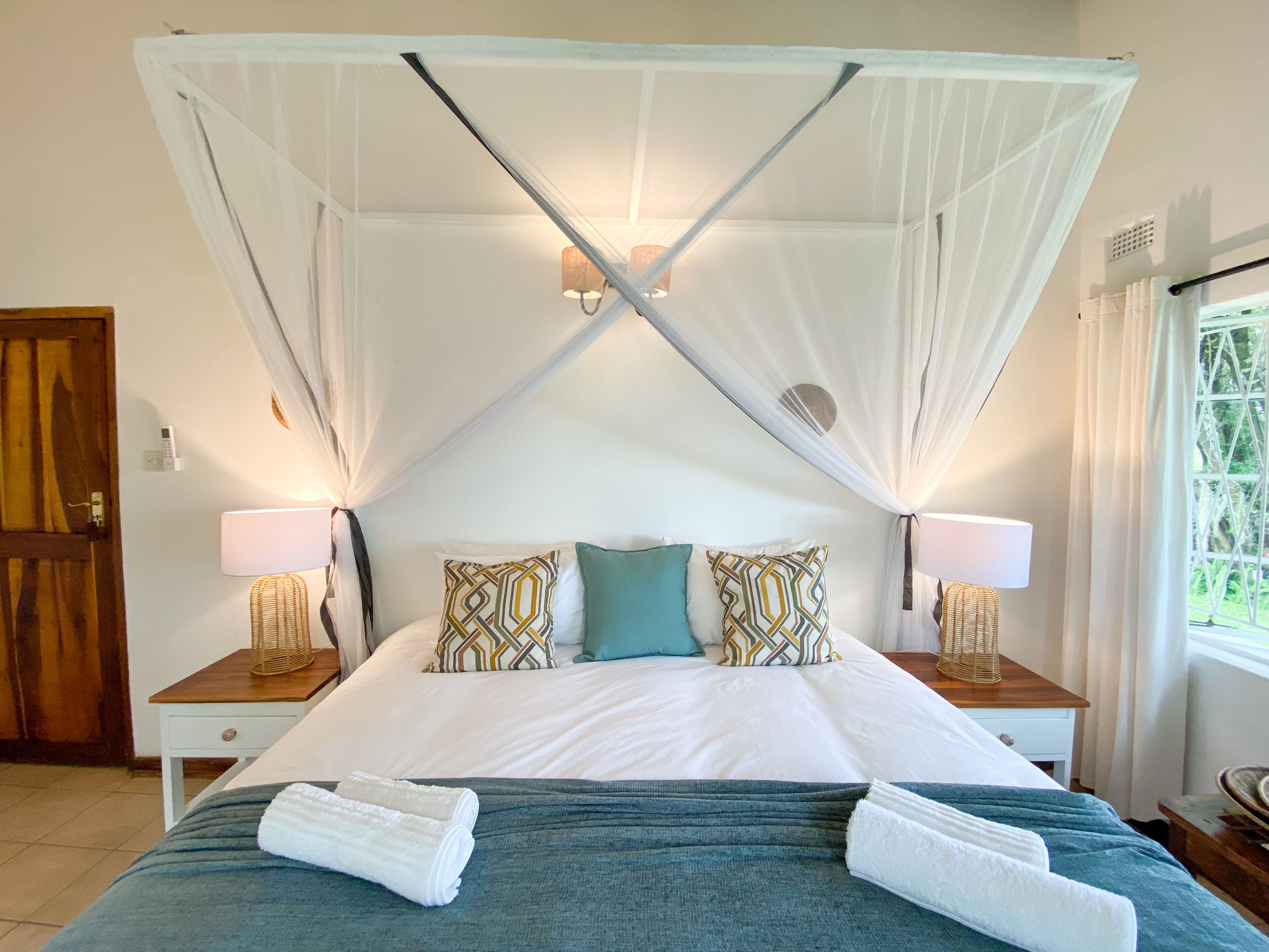 Un dormitorio con cama a dosel, dos lámparas de noche, almohadas estampadas y una cama bien tendida con toallas.