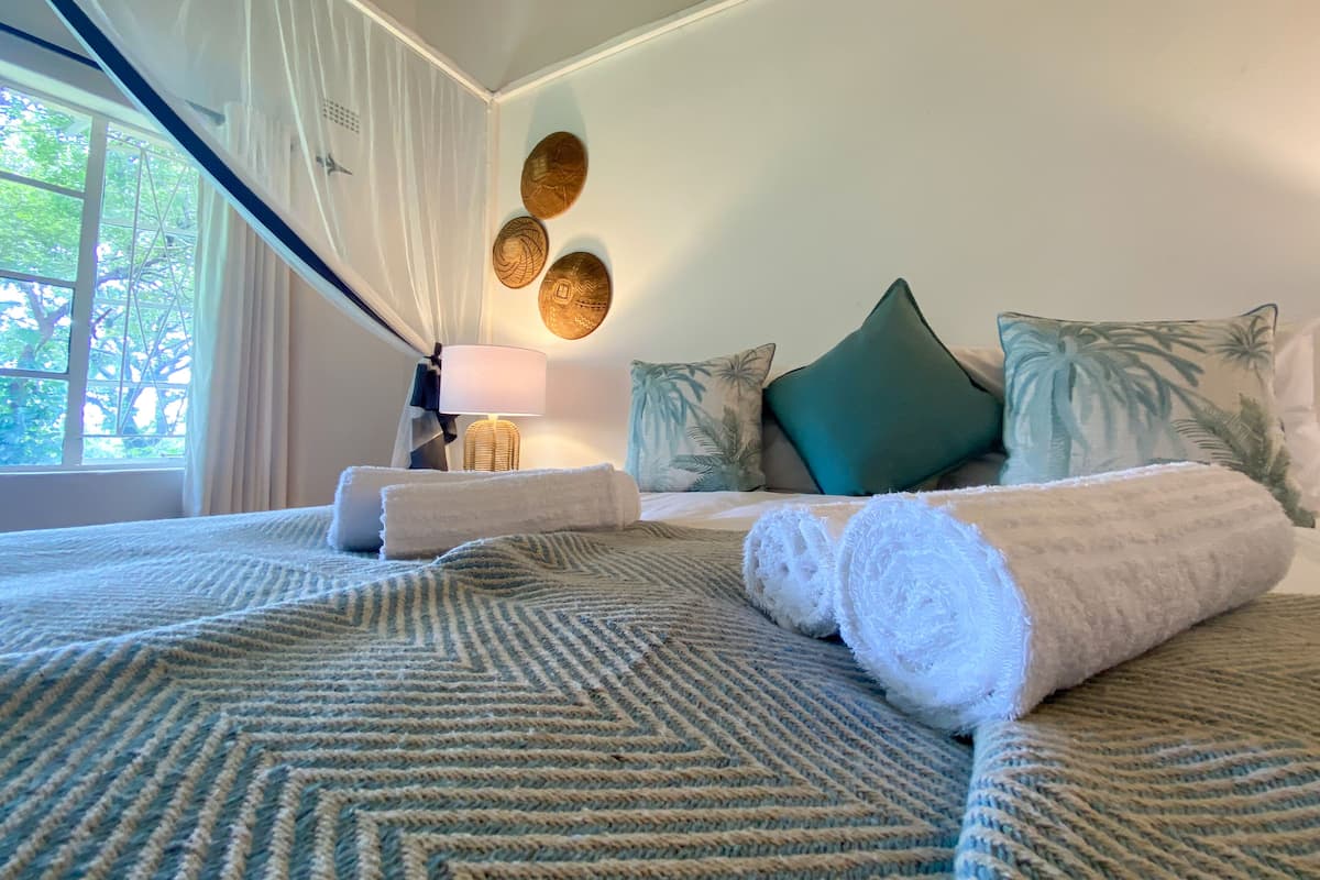A neatly made bed with rolled towels, a bedside lamp, and decorative wall art.
