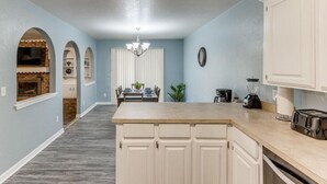 A modern kitchen with a central island, white cabinetry, and a dining area with a chandelier.