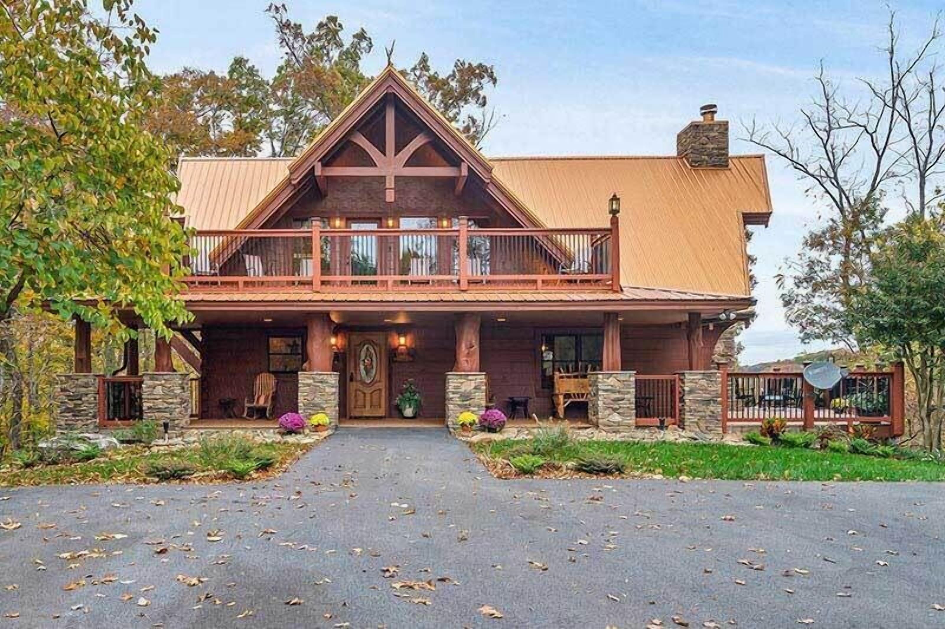 Une grande maison à deux étages, dotée d’un porche avant imposant, de piliers en pierre et d’un balcon en bois.