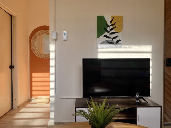 A modern living room with a flat-screen TV, a decorative plant, and a wall-mounted artwork.