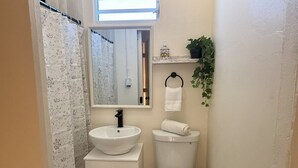 Pieni kylpyhuone, jossa on valkoinen pesuallas, wc-istuin ja peili, joka on sijoitettu pesualtaan yläpuolelle.
