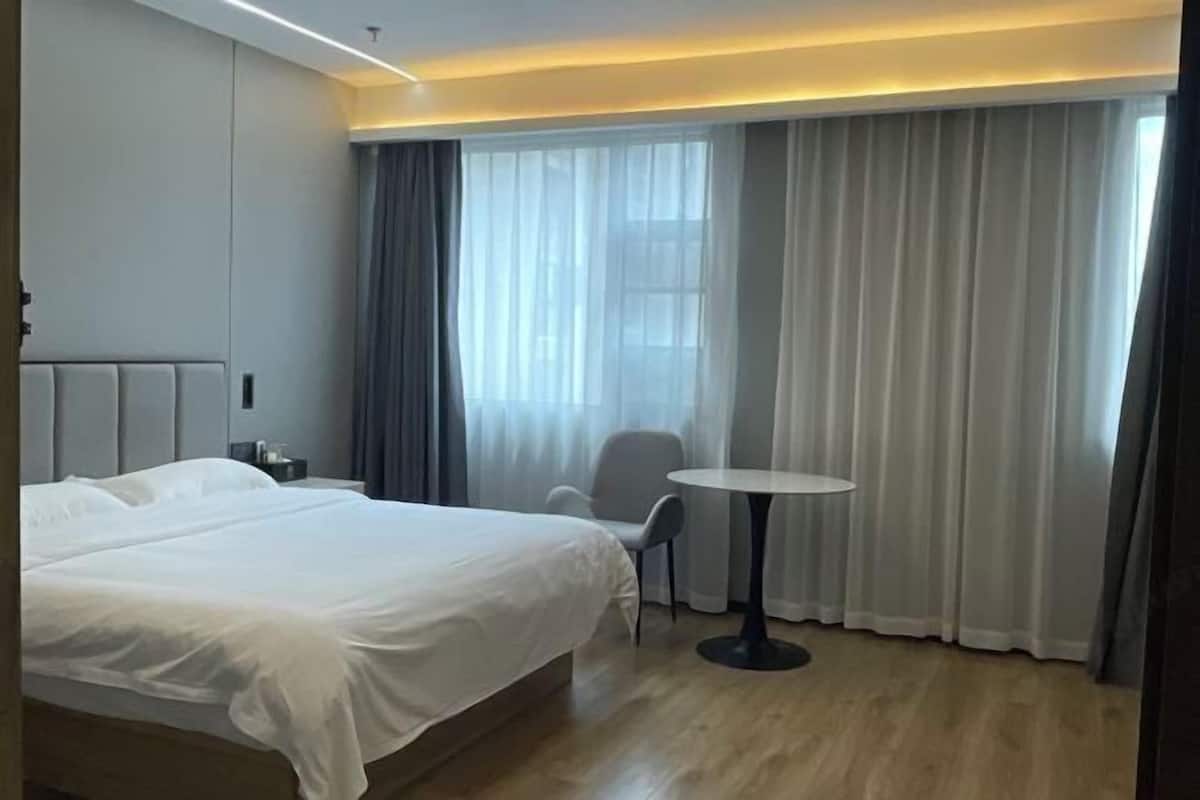 A hotel room with a large bed, a small round table, a chair, and a window with curtains.