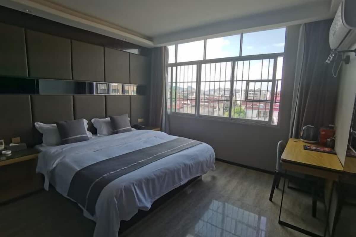 A modern hotel room with a large bed, a desk, and a window with a city view.