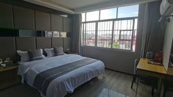 A modern hotel room with a large bed, a desk, and a window with a city view.