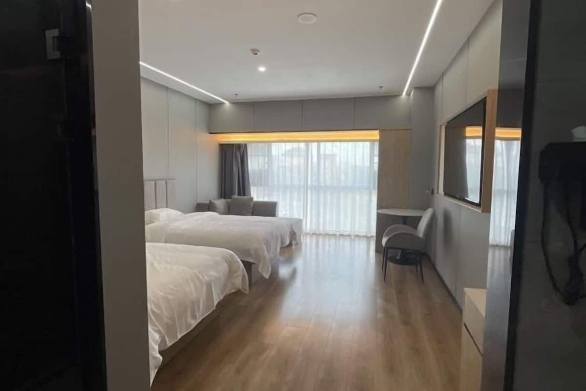 A hotel room with two beds, a desk, a chair, a large window with curtains, and a television.