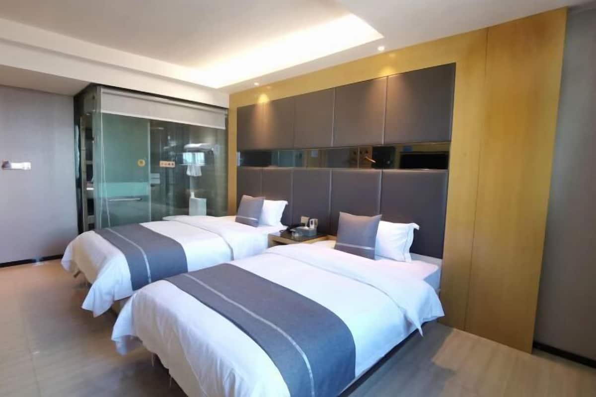 A modern hotel room with two beds, a glass partition, and a built-in wardrobe.