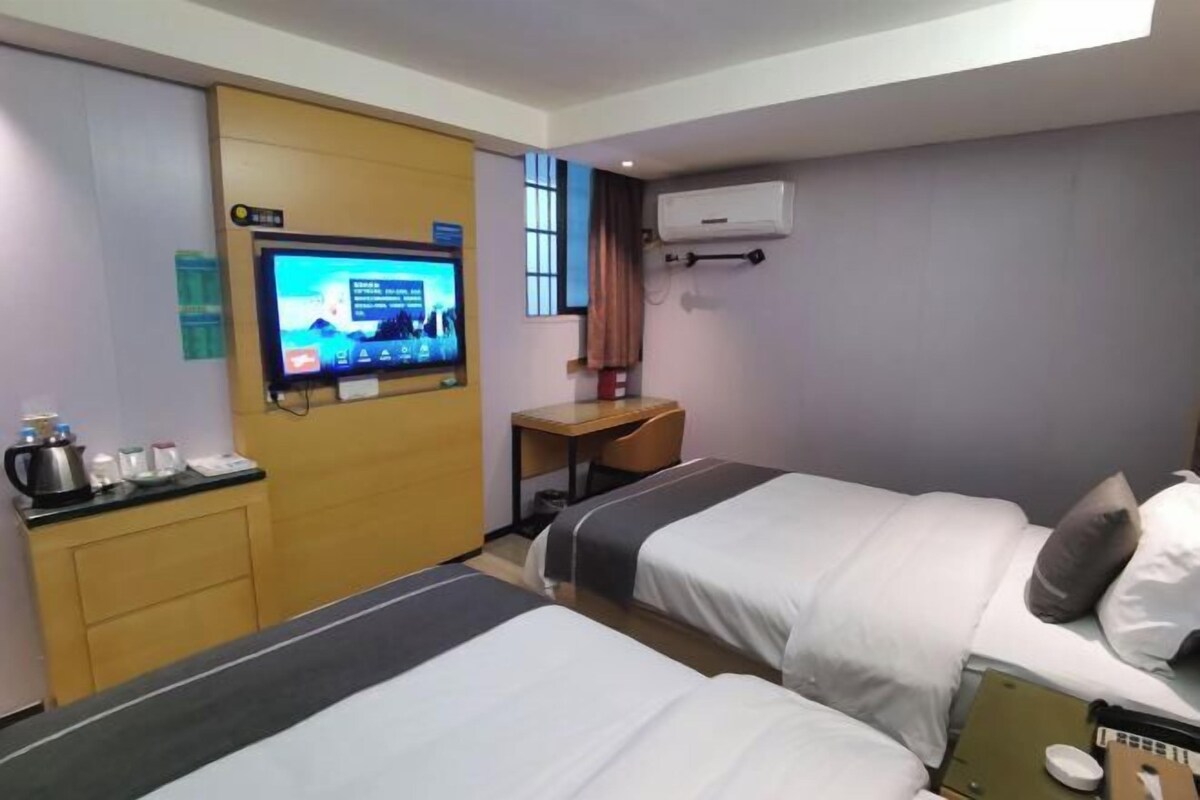 A hotel room with two beds, a desk, a television, and an air conditioning unit.