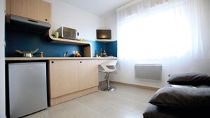 A compact kitchen with a built-in microwave, a small refrigerator, and a bar stool. - Studio Calme et Cosy Bien Équipé (Perpignan)