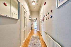 Leading to a space, this hallway features a patterned rug and wall-mounted hooks.