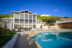 Un hôtel moderne doté d’une piscine, de chaises longues et offrant une vue sur une colline.