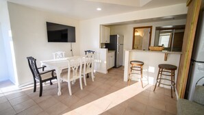 A compact kitchen with a dining area, a TV mounted on the wall, and a small seating area with stools. - Sapala 2 - Oceanfront Poolside Apt w/ Shared Pool (Christiansted)