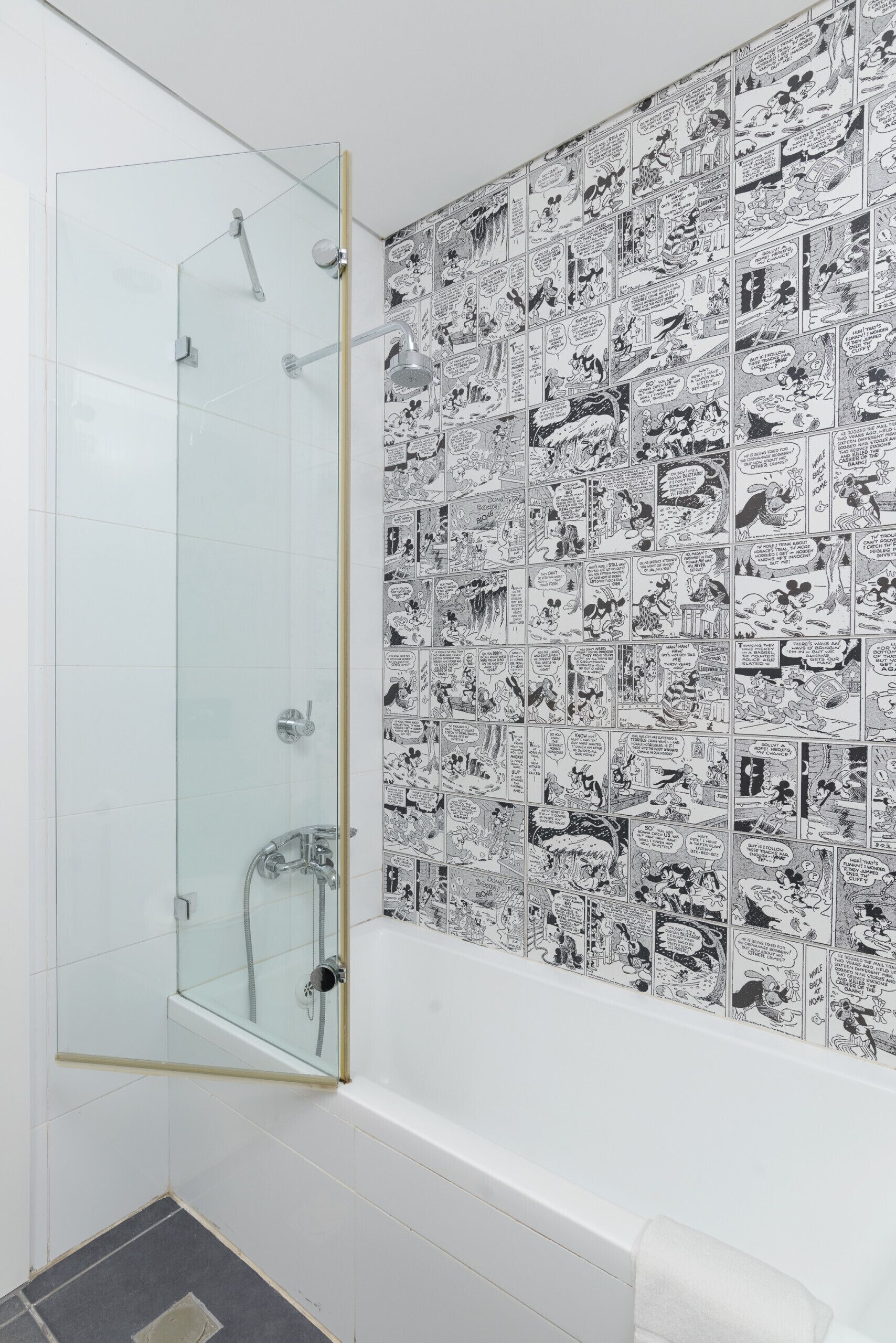 A bathroom with a glass shower enclosure and a wall covered with black and white comic strip tiles.